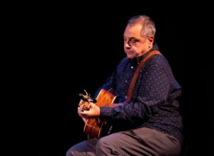 A man sitting in the dark playing a guitar with the light focused on him
